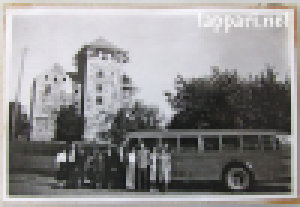Harmaasävyinen valokuva bussista, jonka edustalla rivissä ihmisiä, ja taustalla näkyy Turun linna.